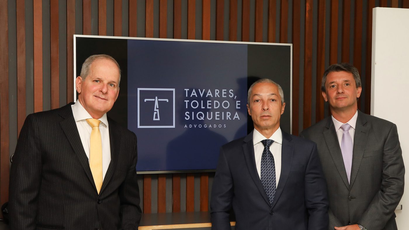 Os três sócios diante do painel com a marca do escritório
