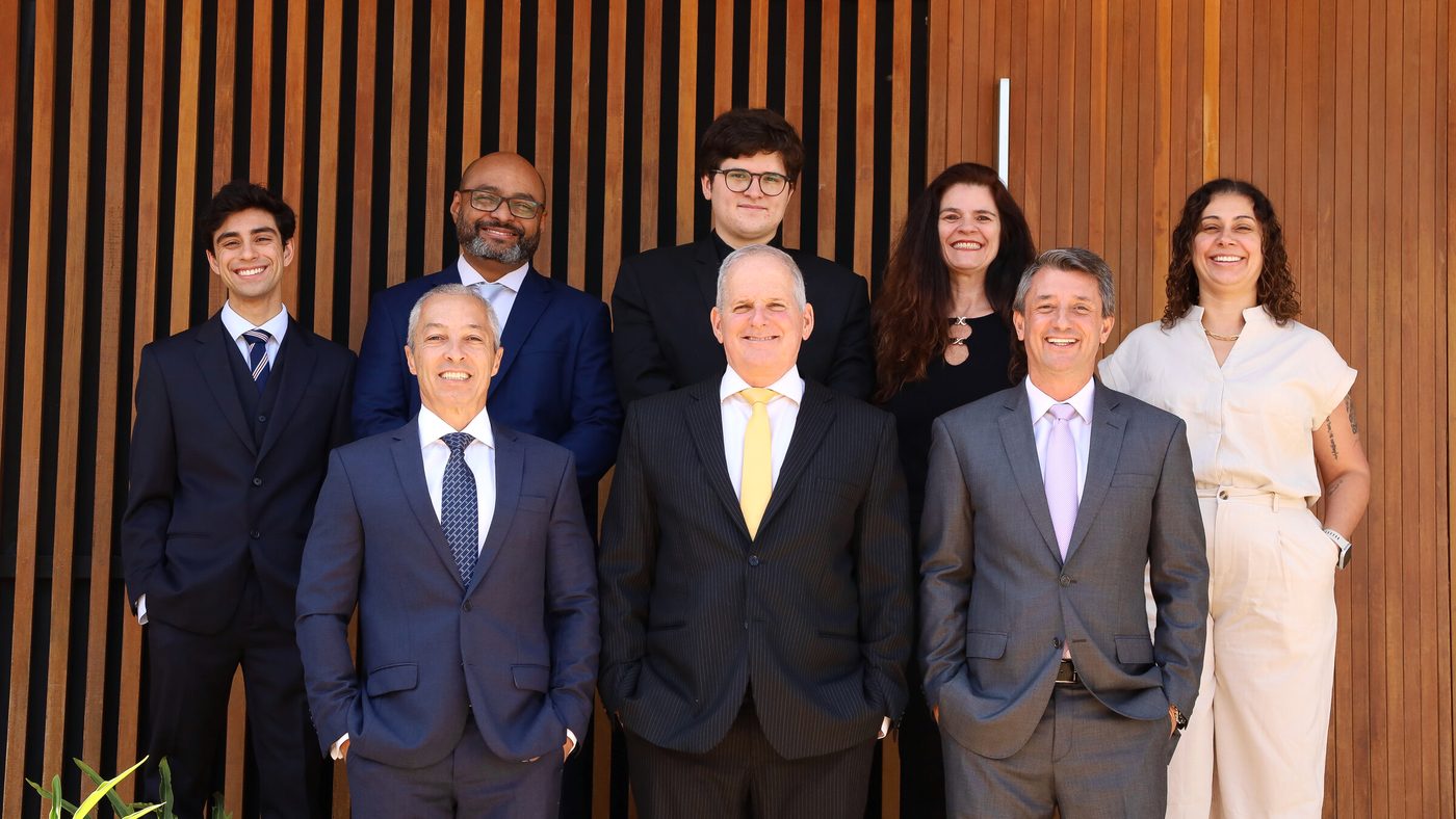 Sócios, advogados e equipe do escritório reunidos diante do painel de madeira da sede