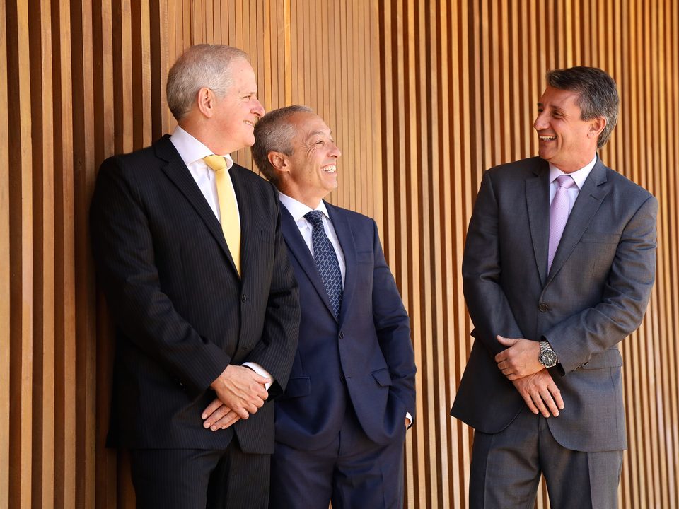 Os três sócios conversando diante do painel de madeira da sede